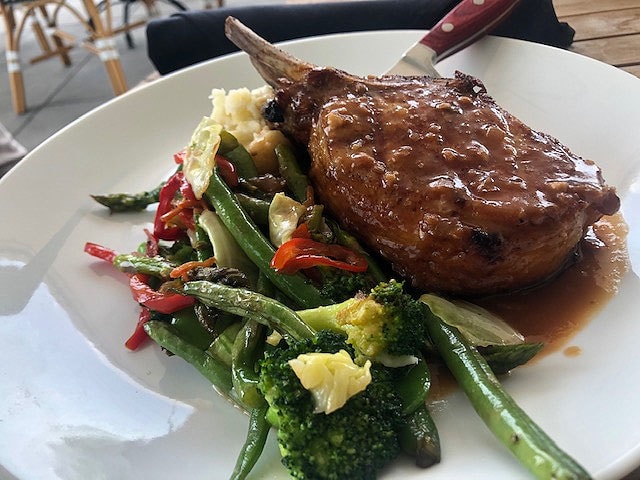 pork chop on white plate with steamed broccoli and green beans